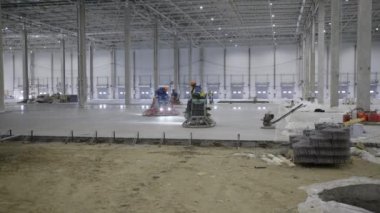 Çalışan işçilerin ve çeşitli makinelerin yer aldığı yoğun bir inşaat sahasının geniş ve ayrıntılı bir görüntüsü. Kırp