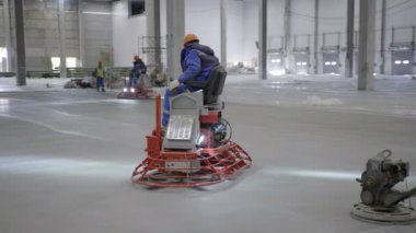 Profesyonel kalifiye işçiler büyük ve geniş bir depo ortamında beton bitirme görevlerini ustalıkla yerine getiriyorlar. Kırp