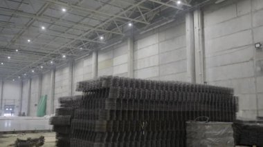 Geniş bir endüstriyel depo, parlak tepe ışıklarıyla aydınlatılmış istiflenmiş materyaller sergiliyor. Kırp