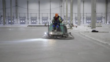 Becerikli bir işçi beton bitirici bir araç kullanır. Büyük bir sanayi bölgesindeki beton yüzeyi titizlikle düzleştirmek için. Kırp