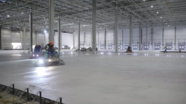 İşçiler bugün geniş bir depo ortamında pürüzsüz beton zemini dikkatlice cilalıyorlar. Kırp
