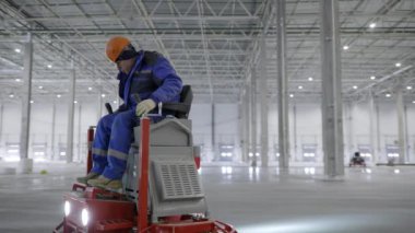 Bir işçi büyük bir inşaat sahasında beton döşemeyi pürüzsüzleştirmek ve bitirmek için ustalıkla makineler kullanır. Kırp