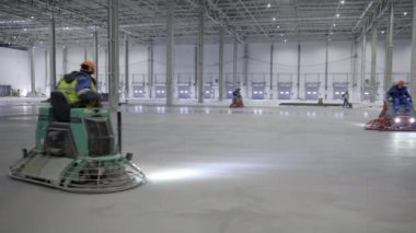 İşçiler, büyük bir sanayi bölgesinde beton zemini verimli bir şekilde döküp bitirmek için makineler kullanıyorlar. Kırp