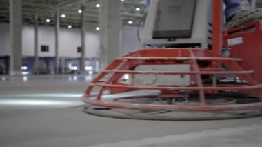 Geniş bir sanayi ortamında yeni dökülmüş zemini düzleştiren modern bir beton bitiş makinesi. Kırp