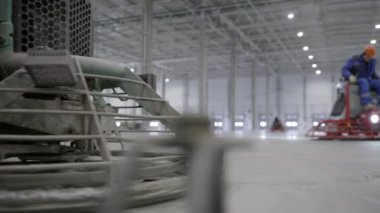 İşçiler, geniş bir depo ortamındaki beton zemini etkili bir şekilde tamamlamak için ağır makineleri ustalıkla kullanıyorlar. Kırp