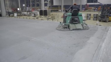Yetenekli bir işçi büyük bir sanayi bölgesindeki yeni döşenmiş betonu bitirmek için troweling makinesi kullanıyor. Kırp