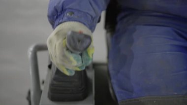 Yakın çekim, bir işçinin koruyucu eldiven giyerken makine kontrollerini sıkıca kavradığını gösteriyor. Kırp