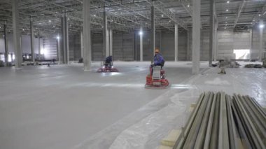 Yetenekli işçilerden oluşan bir ekip geniş bir depoda gelişmiş makinelerle betonu ustalıkla düzleştiriyor. Kırp