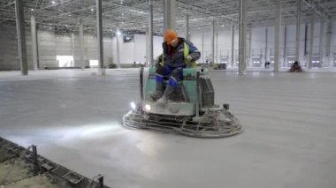 Yetenekli bir işçi büyük, boş bir sanayi binasının beton zeminini tamamlamak için bir güç malası kullanır. Kırp