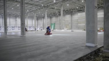 Becerikli inşaat işçileri, pürüzsüz bir yüzey için inşaat halindeki geniş bir depoda beton döşüyorlar. Kırp