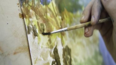 Becerikli bir sanatçı, tuval üzerinde fırçası olan canlı ve renkli bir manzara resminin detaylarını titizlikle anlatır. Eylem