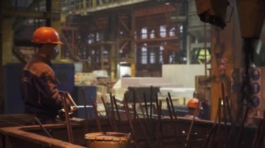 Canlı bir imalat ortamında, kendini işine adamış işçiler ağır makineleri ustalıkla çalıştırırken kask takıyorlar. Menkul Kıymetler