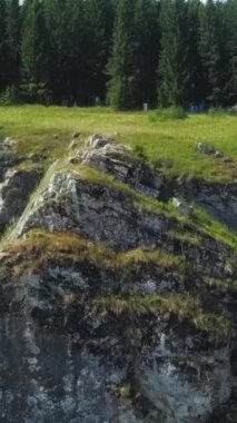 Havadan bakıldığında, canlı yeşillikler ve manzarada yüksek ağaçlarla çevrili engebeli bir kaya oluşumu görülüyor. Kırp