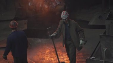 İki deneyimli dökümhane işçisi, yüksek ısıda çalışan bir ortamda erimiş metal akışını ustalıkla yönetiyorlar. Menkul Kıymetler