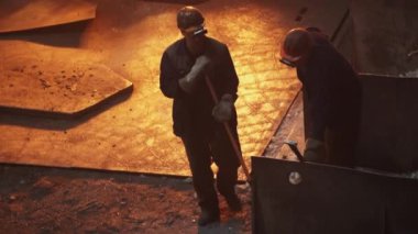Işıl ışıl bir endüstriyel ortamda erimiş metali yöneten iki işçi marifetli işçilik sergiliyor. Menkul Kıymetler