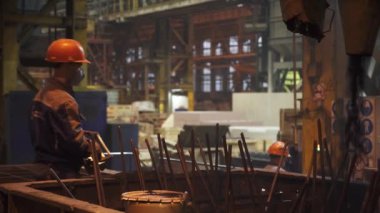 Canlı bir imalat ortamında, kendini işine adamış işçiler ağır makineleri ustalıkla çalıştırırken kask takıyorlar. Menkul Kıymetler