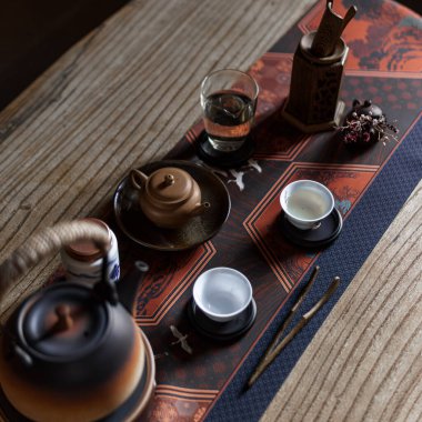 Süslü bir çaydanlık, zarif fincanlar ve kırsal ahşap bir masa üzerindeki geleneksel elementlerle rahatlatıcı bir çay takımı.