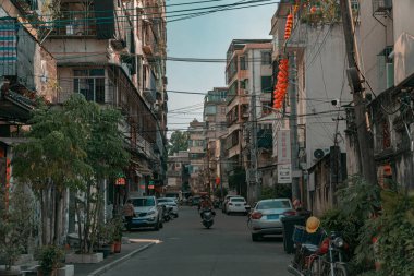 Parlak, berrak bir gökyüzü altında konut binaları ve araçların sergilendiği canlı bir şehir caddesi.