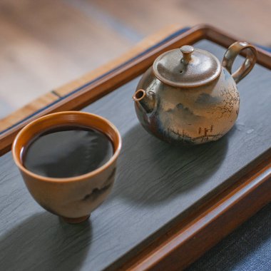 Büyüleyici bir ahşap tepsiye konmuş bir çaydanlık ve fincan arkadaşlarla çay içmek için sakin bir ortam yaratıyor.