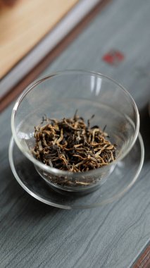 Güzel ahşap bir yüzey üzerinde şeffaf cam bir kâse içinde açık yeşil çay sergilenen detaylı bir yakın çekim görüntüsü.