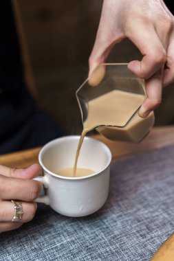 Bir görüntüde krema dumanı tüten bir kahve bardağına dökülüyor, rahat ve rahatlatıcı bir ortam yaratıyor.