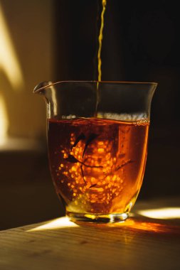 Güzel yansımaları ve zengin kehribar tonlarını sergileyen temiz bir bardağa nazikçe dökülen çayın yakın plan görüntüsü.