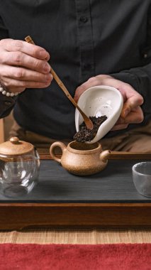 Karmaşık bir çay seremonisinin yakın plan görüntüsü, çay yapraklarının dikkatlice çaydanlığa dökülmesi.