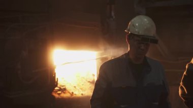 Çelik fabrikasında çalışan bir işçi, tam teçhizatlı, parlayan erimiş bir metal zeminine karşı konumlandırılmış. Menkul Kıymetler