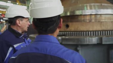 Bir sanayi işçisi, bir üretim tesisi içinde ağır makinelerin çalışmasını dikkatle izliyor. Menkul Kıymetler