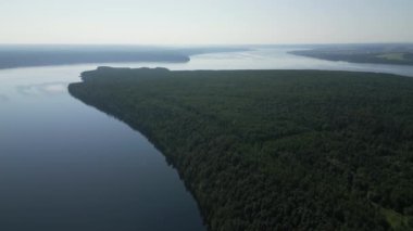 Sakin bir nehrin kıyısında geniş yeşil bir ormanı güzel bir şekilde yakalayan nefes kesici, sakin bir hava görüntüsü. Kırp