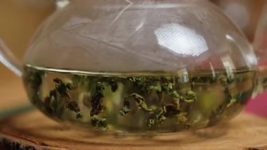 Bitkisel çayın çok güzel demlendiği detaylı bir yakın plan, cam bir demlikteki canlı yeşil yaprakları vurguluyor. Medya