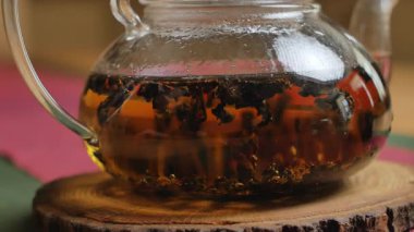 Bu video, sıcak bir ahşap zemin üzerinde zengin çay yaprakları olan cam bir çaydanlık ile huzurlu bir atmosfer yaratarak rahatlamayı yakalıyor. Medya