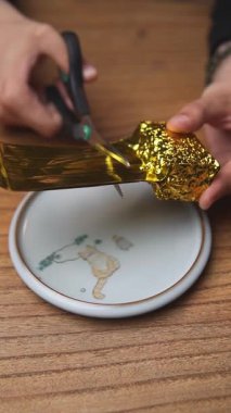 Parlak altın folyo kullanarak muhteşem bir dekoratif plaka hazırlayan eller DIY yaratıcılığının özünü gözler önüne seriyor. Medya