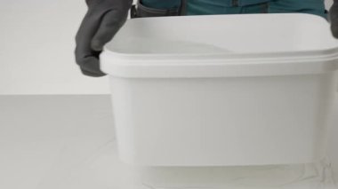 Bu videoda, siyah eldivenli bir kişi, temiz bir çalışma alanındaki beyaz plastik bir kabın açılışını gösteriyor. Yaratıcı