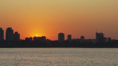 Nefes kesici bir günbatımı, sakin sularda güzel bir şekilde yansıtılan geniş şehir silueti üzerinde canlı renkler bırakır. Medya