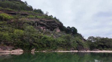 Bereketli yeşil tepelerin bulutlu bir gökyüzünün altındaki sakin suyu güzel bir şekilde yansıttığı huzurlu ve huzurlu bir manzara. Medya