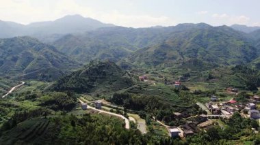 Bu çarpıcı hava manzarası, sakin ve huzurlu bir kırsal bölgenin yanında canlı yeşil dağlar sergiliyor. Medya