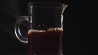 Kahveyle dolu cam bir sürahi, koyu bir zemine karşı zengin renkler ve kabarcıklar sergiliyor. Medya