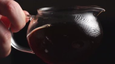 Nefis bir yakın plan çekimde bir el, cam çaydanlığı nazikçe tutuyor. İçi koyu demlenmiş çay dolu. Medya