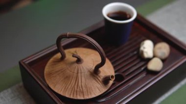 İçinde el yapımı kil çaydanlık, uyumlu bir bardak ve ahşap tepside dekoratif taşlar olan sakin bir çay seti. Medya