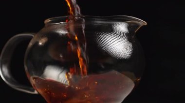 Hoş aromatik çayın büyüleyici bir görüntüsü şeffaf bir çaydanlığa, koyu bir arka plana nazikçe dökülüyor. Medya