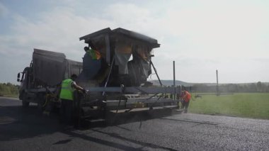 Kendini işine adamış ve çalışkan bir ekip, ağır inşaat makineleri kullanarak asfalt ile yeni bir yol açıyor. Kırp