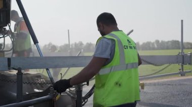 Çok yetenekli bir inşaat işçisi, açık ve mavi gökyüzünün altındaki hareketli bir yol alanında ustalıkla ağır ekipmanları idare ediyor. Kırp