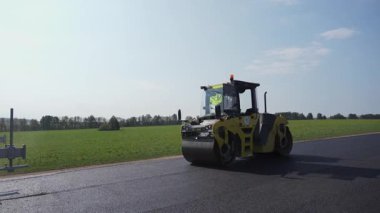 Ağır bir patenci, verimli yeşilliklerle çevrili manzaralı ve pitoresk bir yolda asfaltı sıkıştırır. Kırp