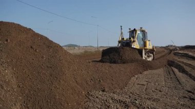 Engebeli bir buldozer araziyi ustalıkla yeniden şekillendiriyor, çeşitli inşaat ve toprak taşıma faaliyetlerini gösteriyor. Kırp