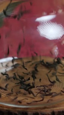 Huzurlu bir sahnede, ahşap bir bardak altlığında, bol miktarda siyah çay dökülen camdan bir çaydanlık görülüyor. Çay yapraklarının güzelliğini ve sakinleştirici demleme ritüelini yakalar. Medya