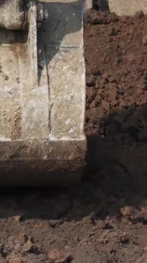 Bir kazı kovası, bir inşaat alanında ağır makineler sergileyerek kazma harekatına girişiyor. Kırp