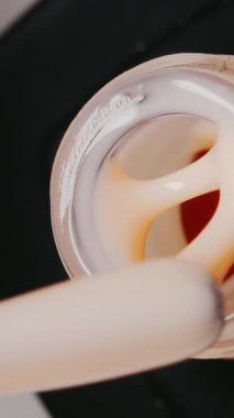 Renkli arka planda krem jöle tırnak cilası. Medya. Son derece yakın çekim. Cilalı fırça şişenin kenarında hareket eder, vernik yavaşça süzülür.