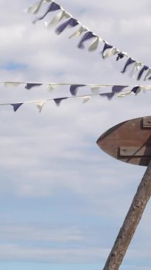 Beyaz, rüzgarda uçuşan mor bir kanat. Bulutlu mavi gökyüzü. Asılı çelenkler. Beyaz - mor kurdeleler havada gelişir. Bayraklar. Tatil dekorasyonu. Durağan video.