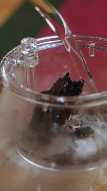 Bu sakin videoda çay hazırlama, bir insan olarak açık çay yapraklarıyla dolu şeffaf bir çaydanlığa sıcak su dökerek canlı renkler ortaya çıkarıyor. Medya